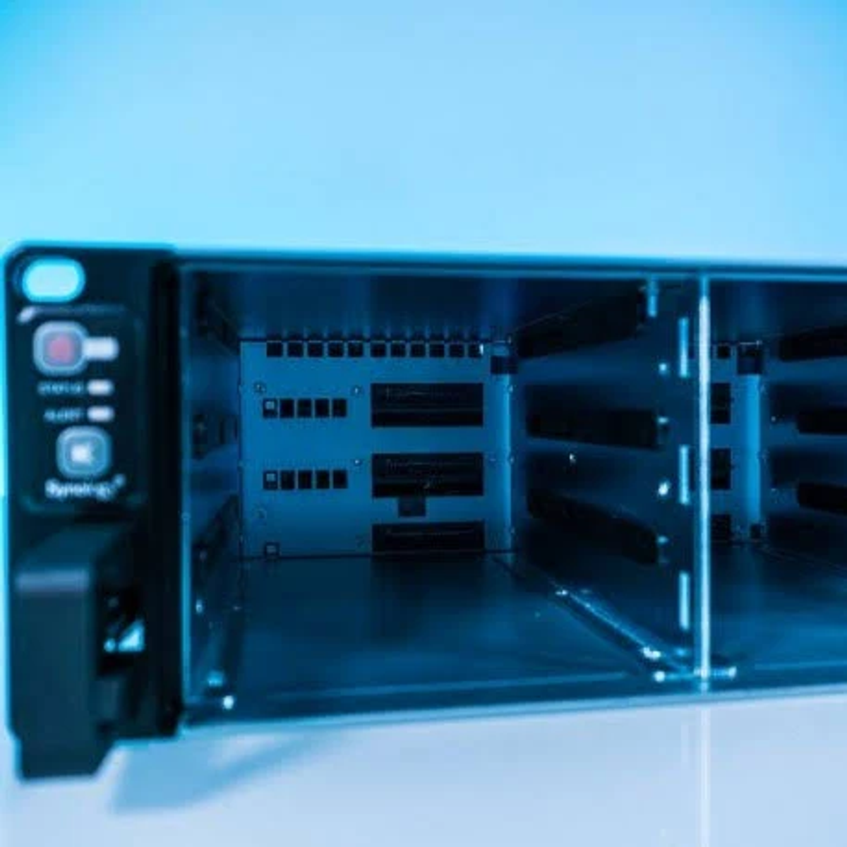 Baie de serveur ouverte. Intérieur d'un serveur avec des emplacements vides pour les disques. Fond bleu.