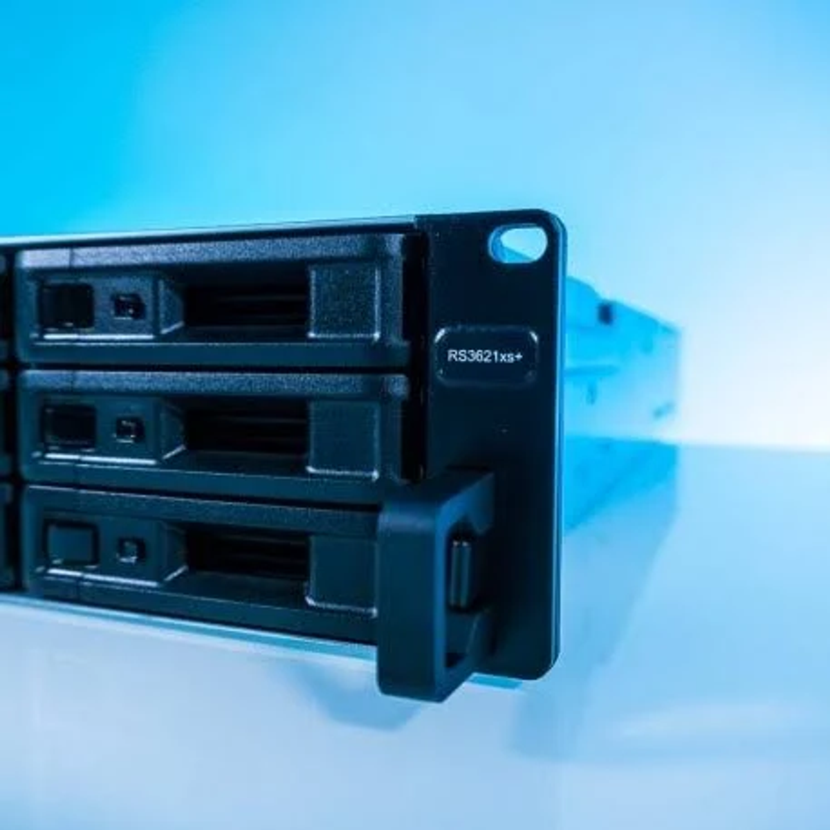Gros plan des baies de lecteur du serveur. Portes noires. Nom du modèle RS3621xs+. Fond bleu.