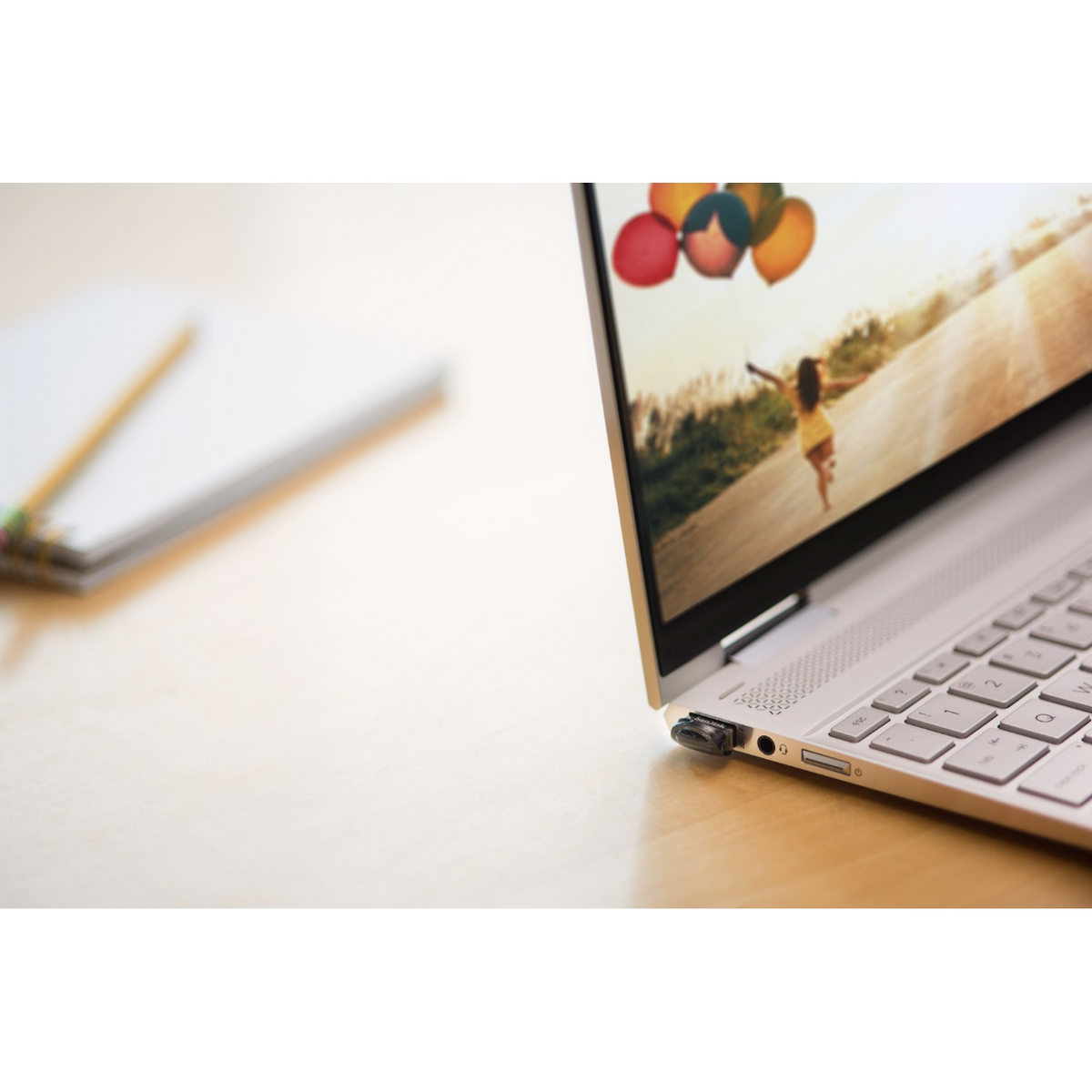 Laptop z podłączonym pendrive'em, wyświetlający obraz. Na stole leżą również notatnik i ołówek.