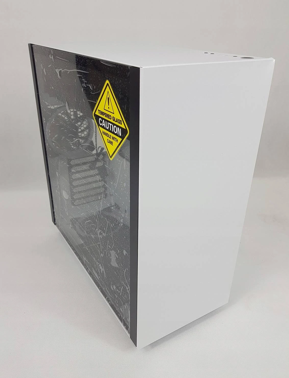 Biała obudowa komputera z bocznym panelem szklanym i naklejką ostrzegawczą. Białe tło.