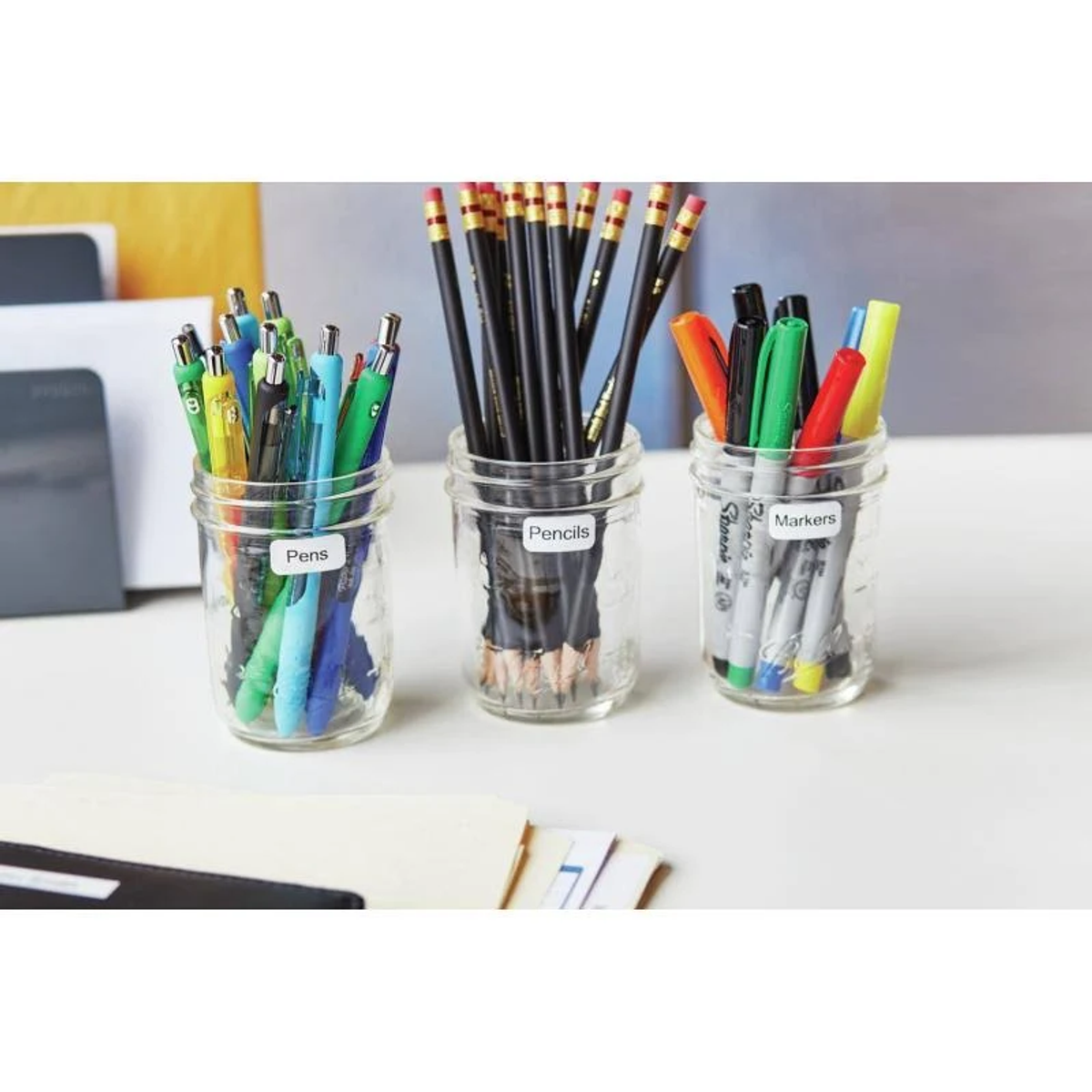 Trois bocaux avec stylos, crayons et marqueurs. Chaque bocal a une étiquette avec le contenu.
