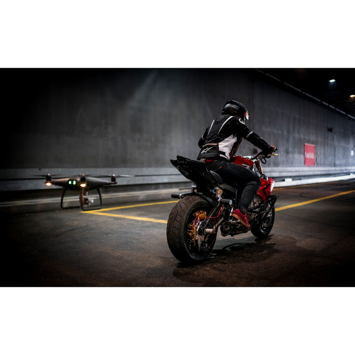 Motocykl na drodze, dron w powietrzu. Betonowe podłoże, ciemne tło.