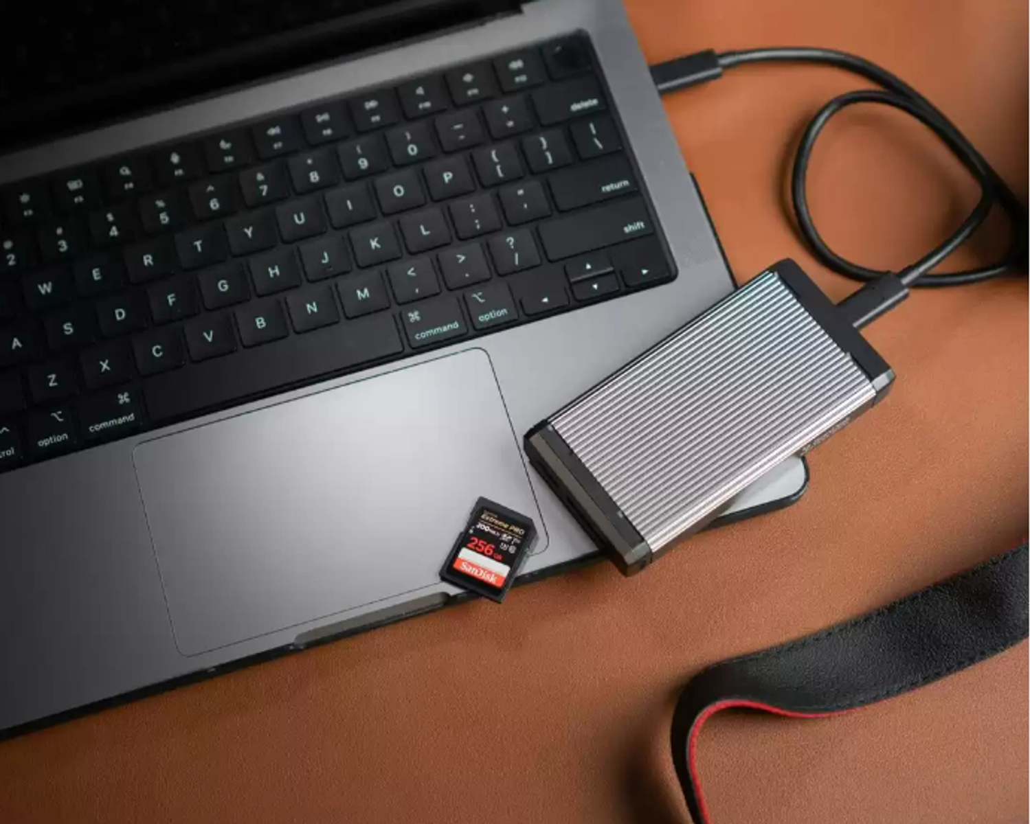 Klawiatura laptopa z dyskiem twardym i kartą SD na brązowej powierzchni, połączona czarnym kablem.