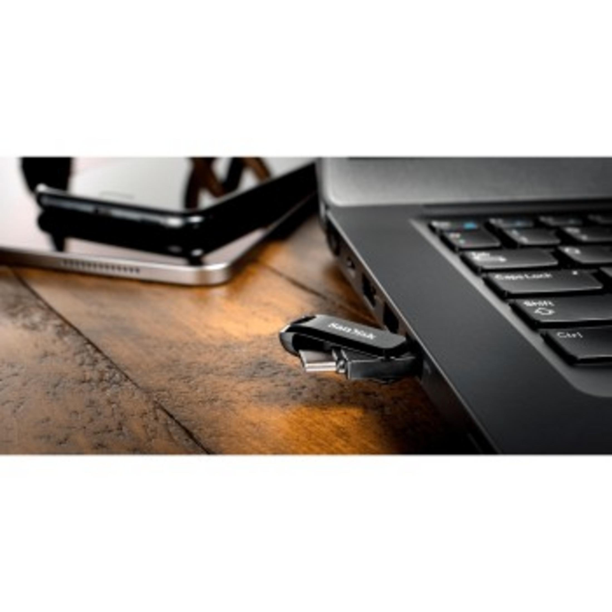 Unidad USB insertada en un portátil, junto a un teléfono en una mesa.