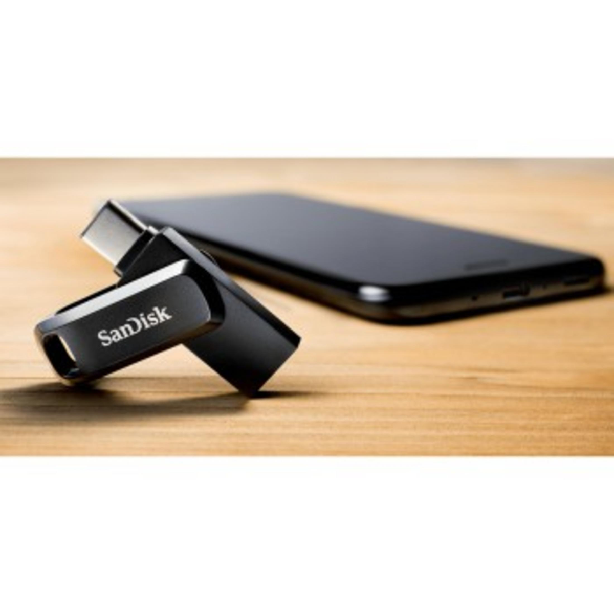 Una unidad flash SanDisk negra junto a un teléfono inteligente negro sobre una superficie de madera.
