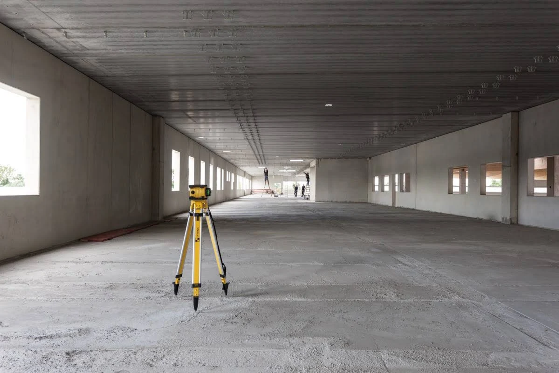 Interno di un grande edificio in cemento armato in costruzione. Un livello laser giallo su un treppiede.