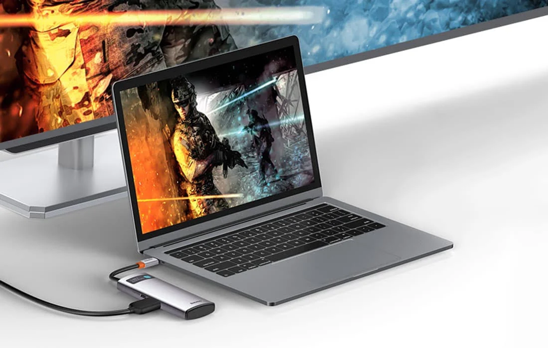 Ein Laptop, der mit einem Monitor und einem USB-C-Hub verbunden ist. Der Laptop zeigt ein Spiel. Der Hub ist silber und klein.