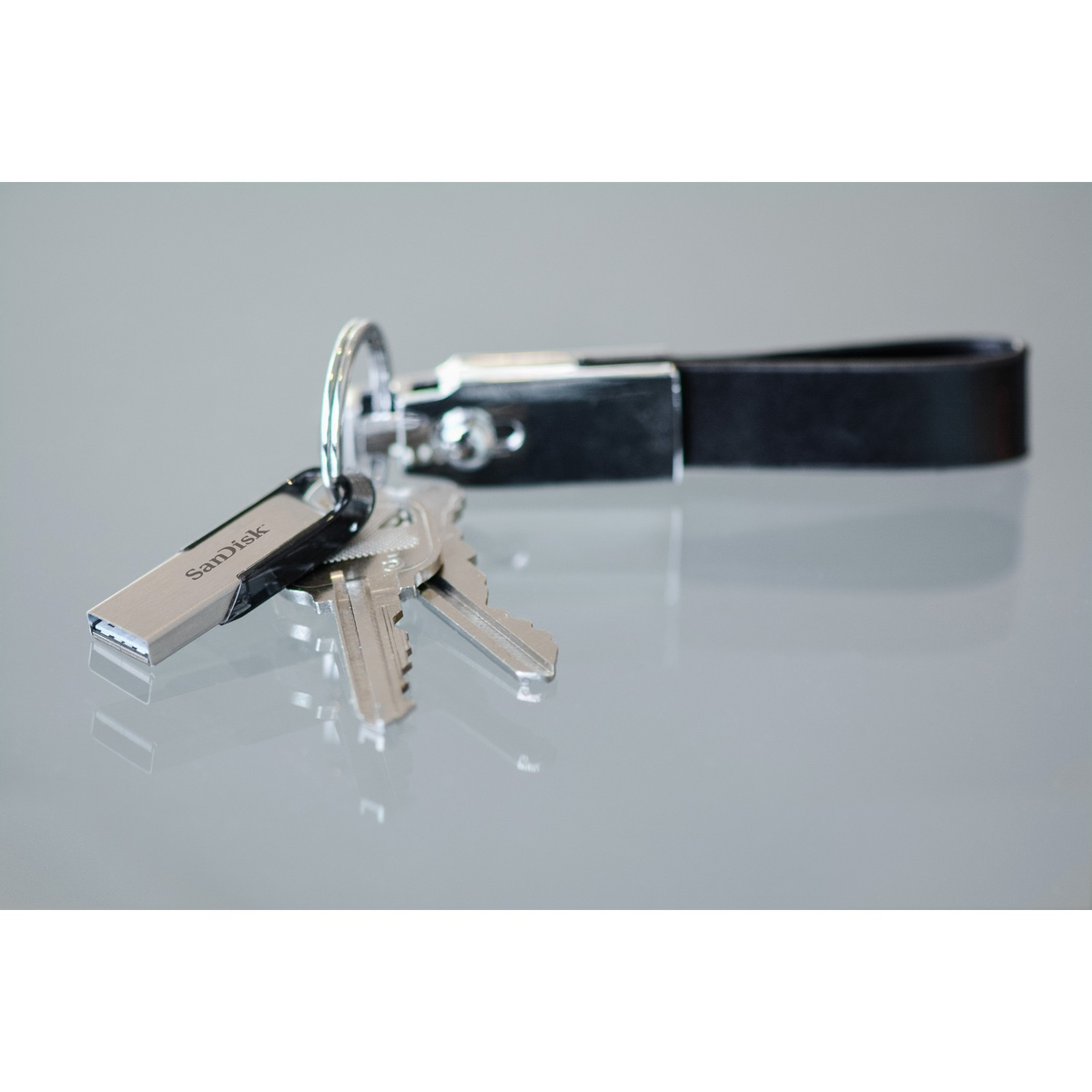 Llaves y una unidad USB con un llavero. La unidad USB es plateada con SanDisk impreso.
