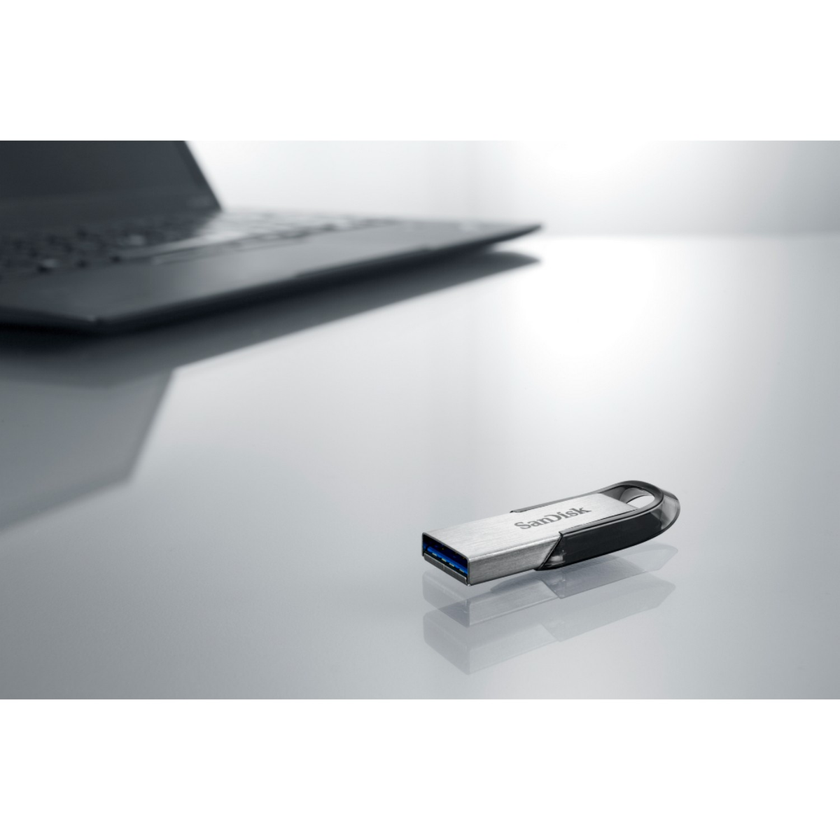 Una unidad flash USB en una superficie reflectante. Una computadora portátil está en el fondo.