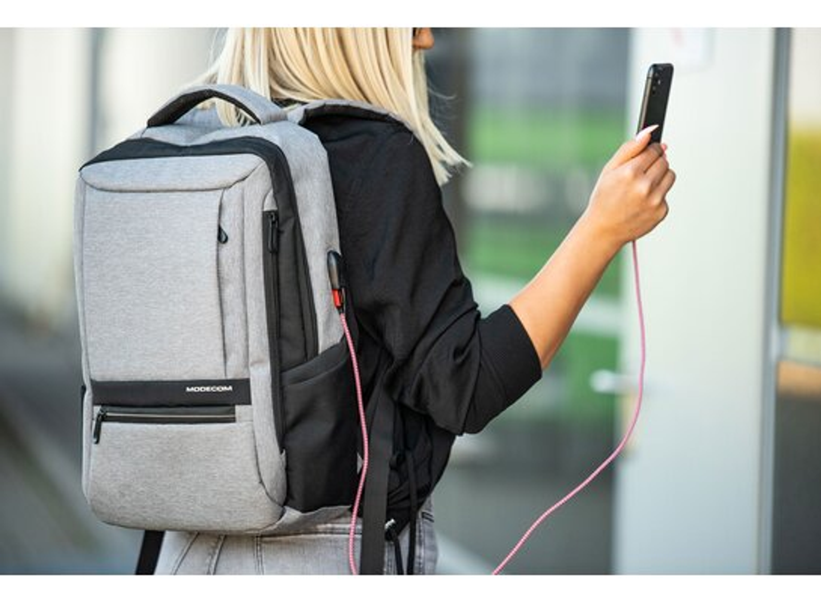 Osoba z plecakiem korzystająca z telefonu podłączonego do niego.