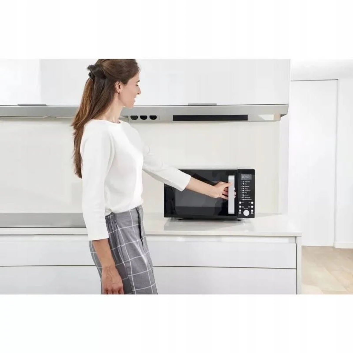 Kobieta używa czarnej kuchenki mikrofalowej w białej kuchni.
