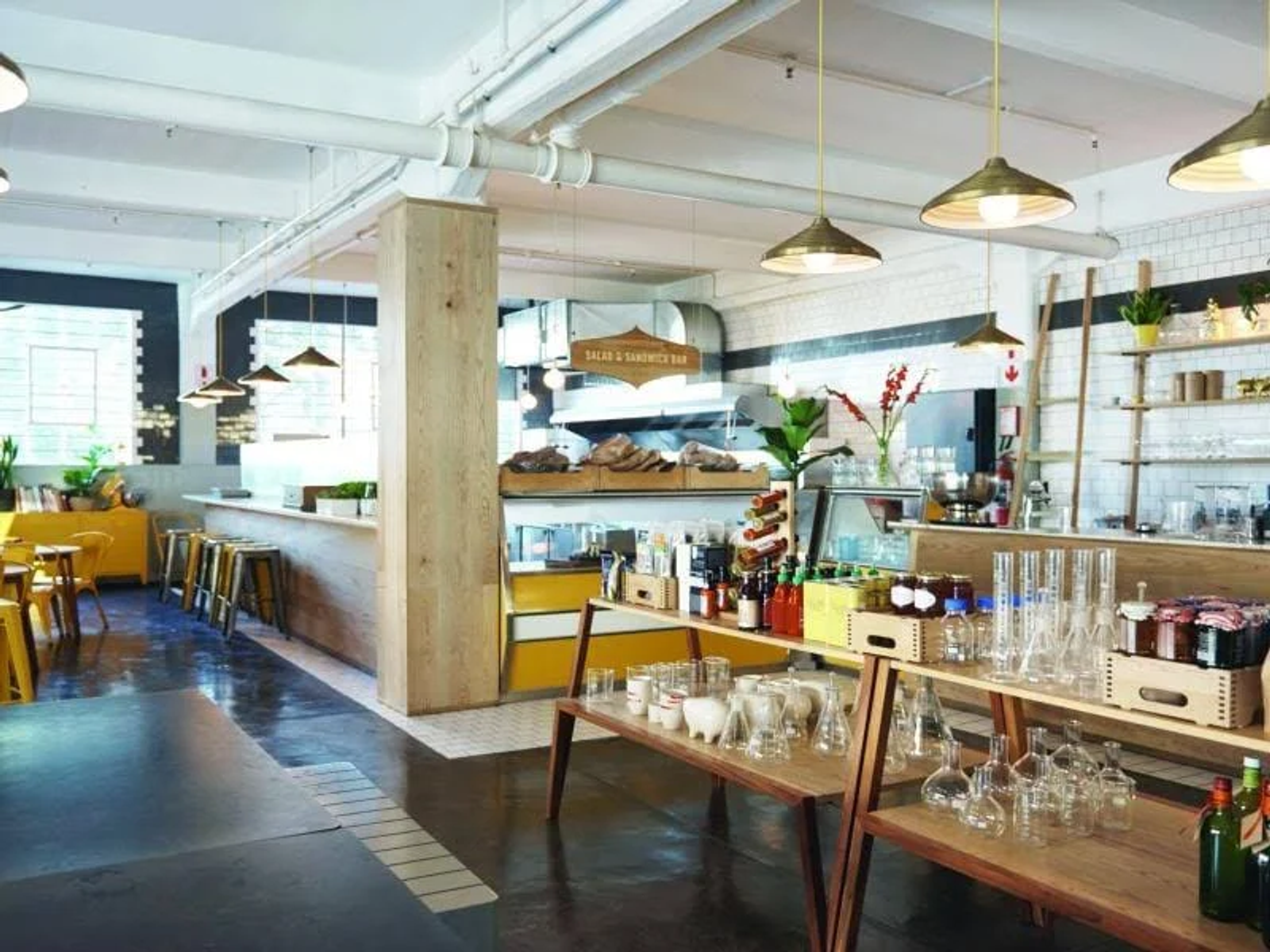 Interior de cafetería con mesas, bar y estanterías. Productos en exhibición.