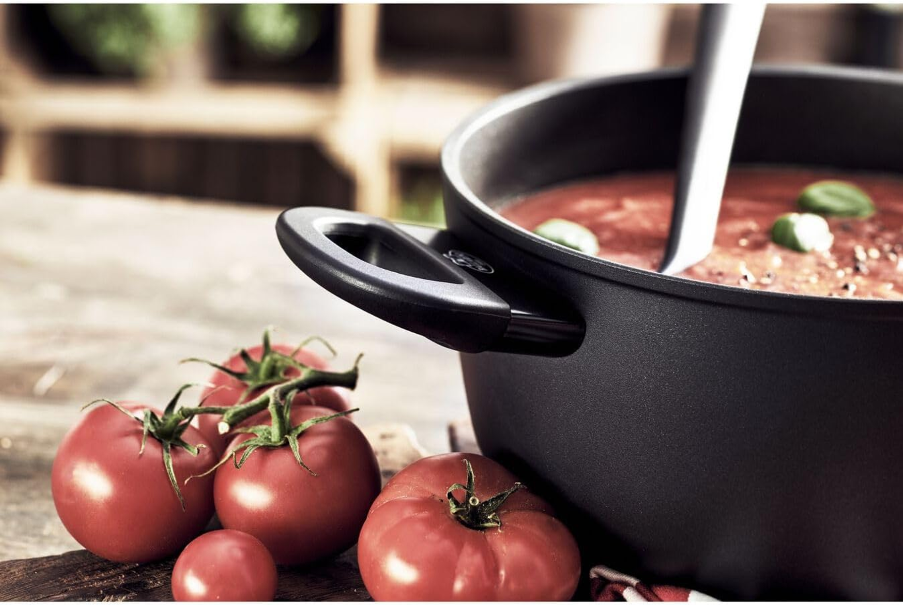 Schwarzer Topf mit Tomatensuppe und Tomaten. Der Topf steht auf einer Holzoberfläche. Ein Löffel ist in der Suppe.