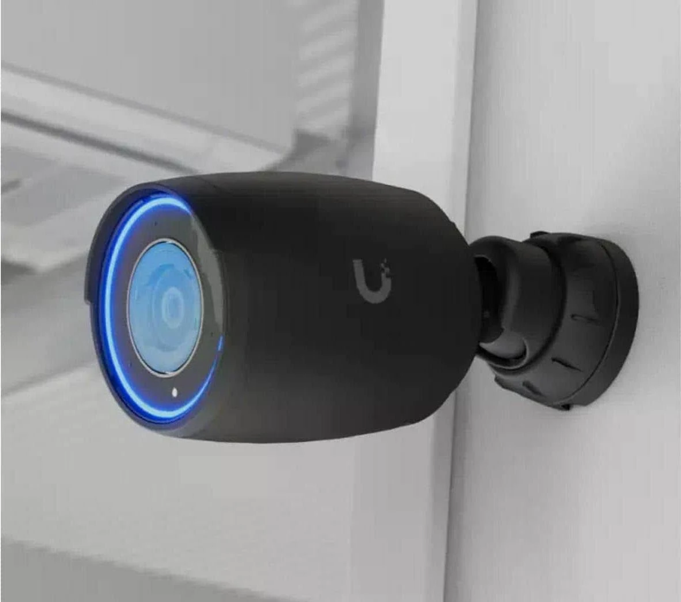 Czarna zewnętrzna kamera bezpieczeństwa zamontowana na ścianie. Ma niebieskie światło wokół obiektywu.