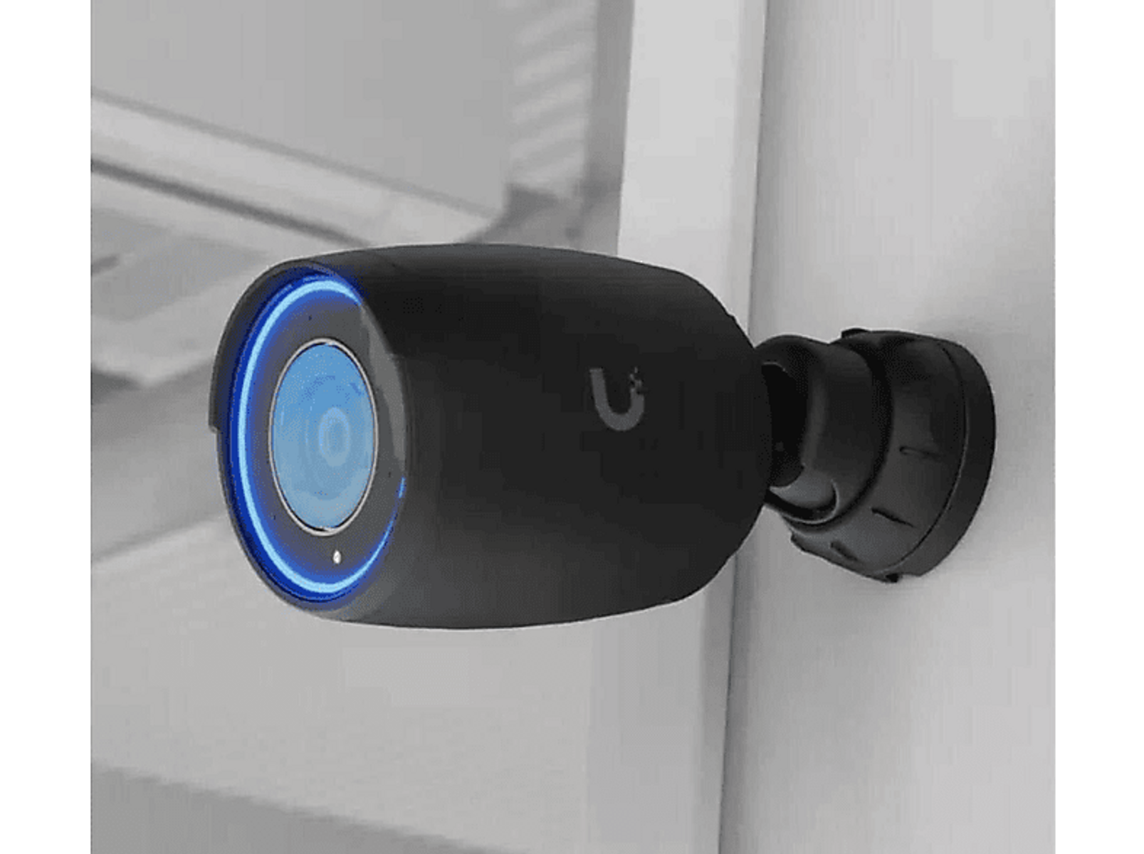 Czarna kamera bezpieczeństwa z niebieskim światłem na białej ścianie, widok z boku.