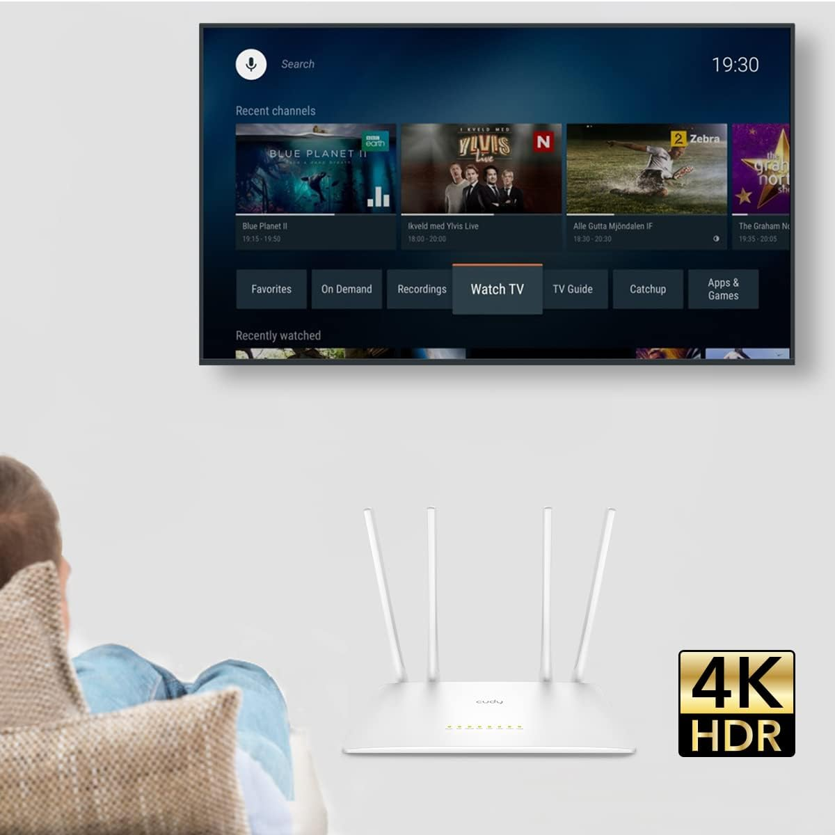 Person schaut fern. Router und Fernseher im Vordergrund. Fernseher zeigt Streaming-Inhalte.