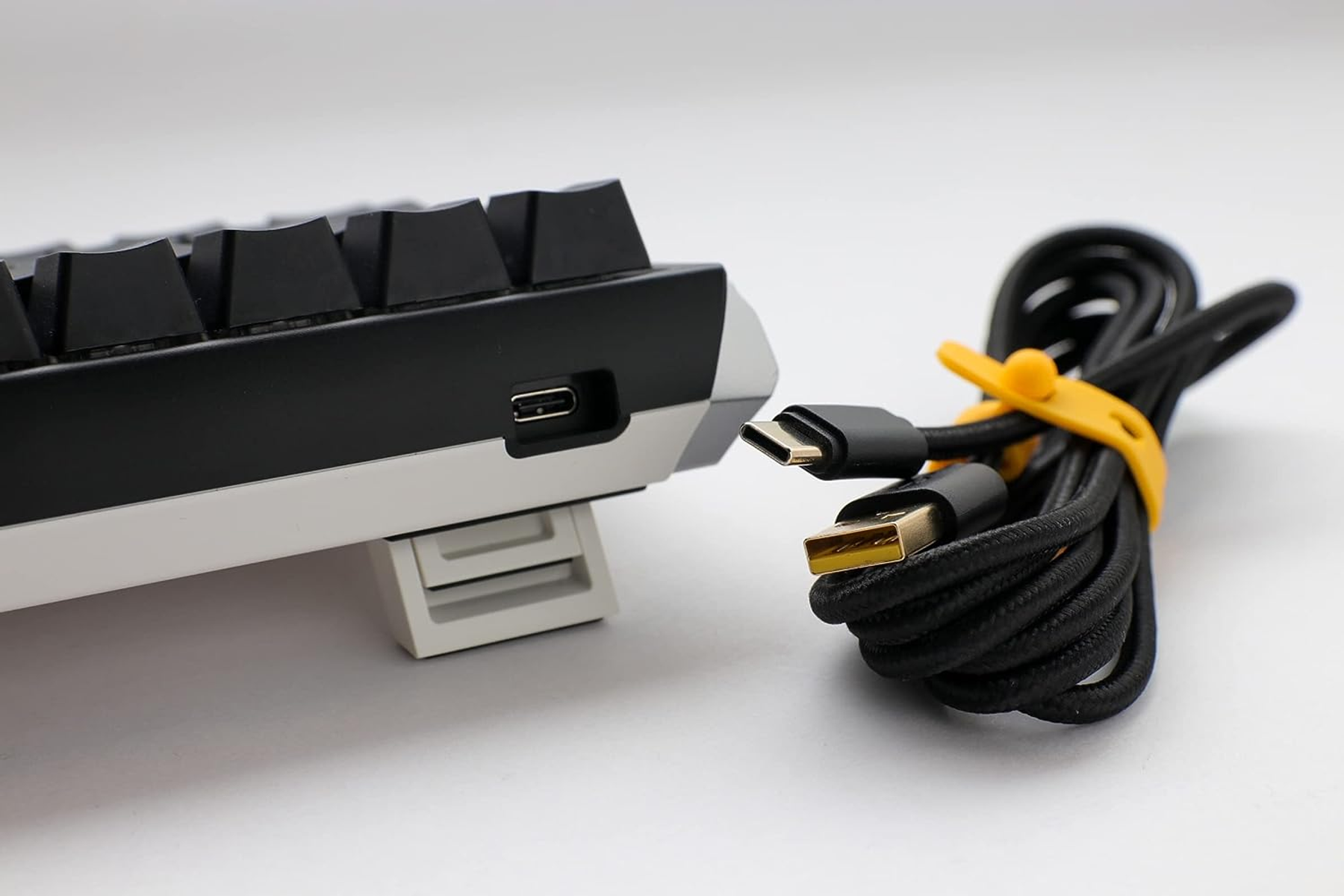 Close-up van een toetsenbord met USB-C-poort en een zwarte gevlochten kabel met gele band.