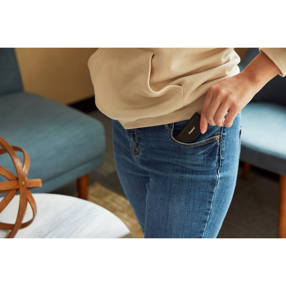 Osoba wkładająca czarny dysk SSD Kingston do kieszeni dżinsów, w tle stół.