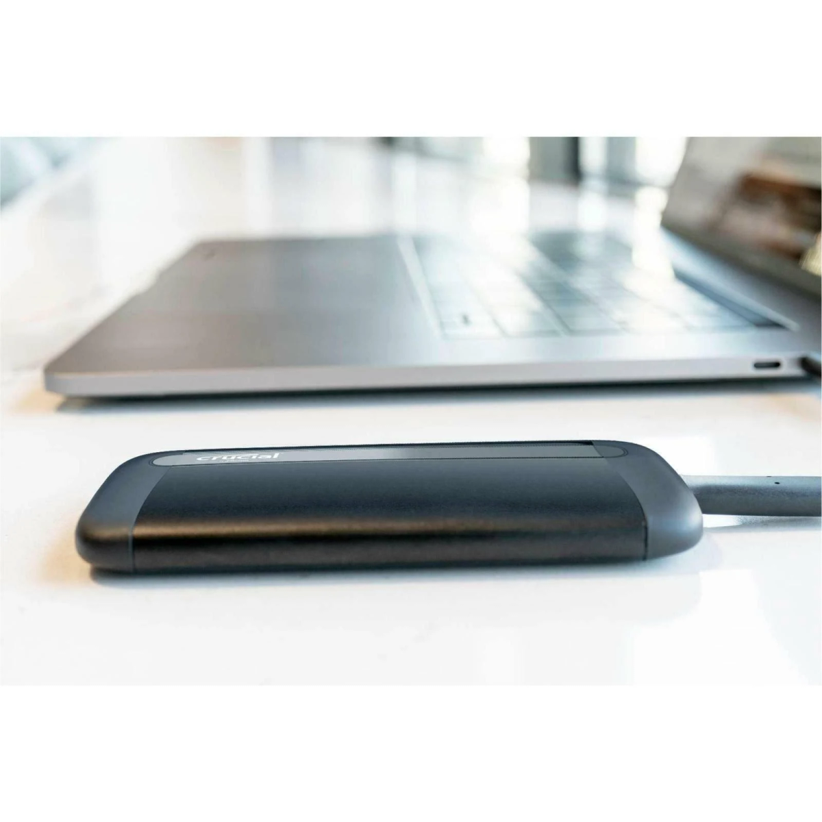 Schwarze SSD, die mit einem Laptop verbunden ist. Die SSD befindet sich auf einer weißen Oberfläche.