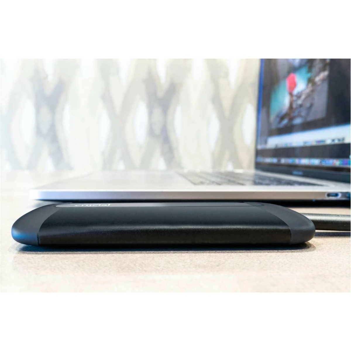 Czarny zewnętrzny dysk SSD obok laptopa. Dysk SSD leży na stole i jest podłączony kablem.