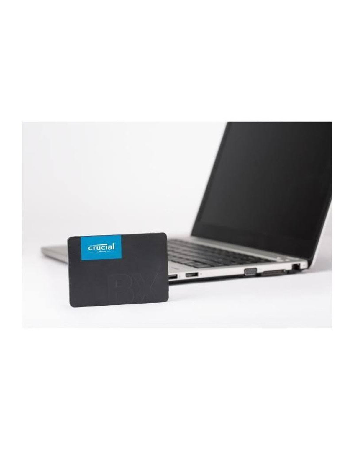Dysk SSD Crucial BX obok otwartego laptopa na białej powierzchni.