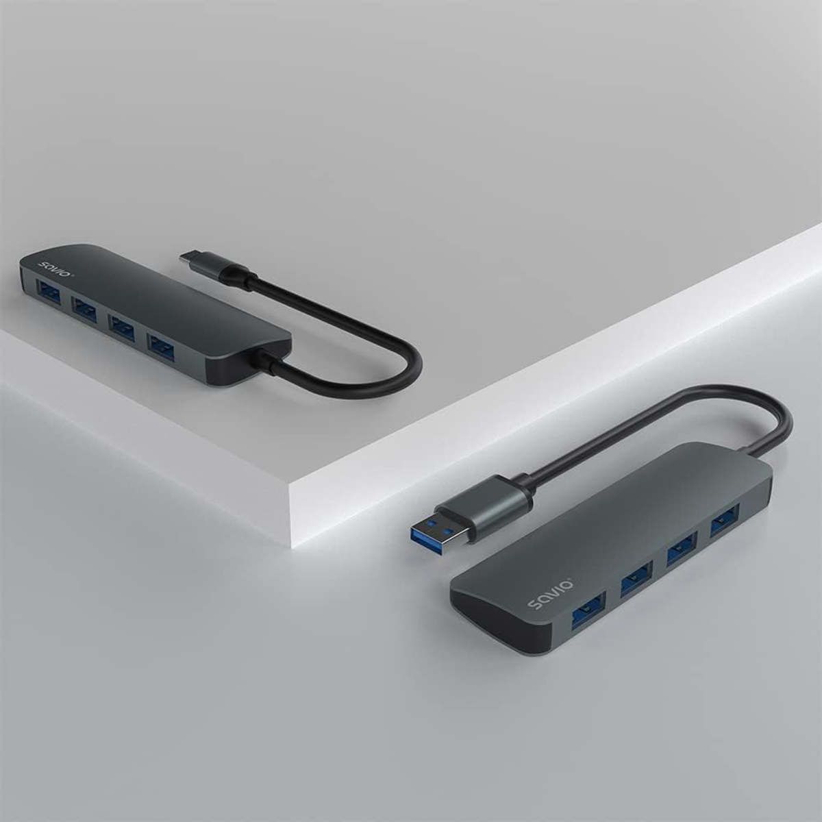 Zwei graue Savio USB-Hubs mit mehreren Anschlüssen, verbunden mit Kabeln. Sie liegen auf einer weißen Oberfläche.