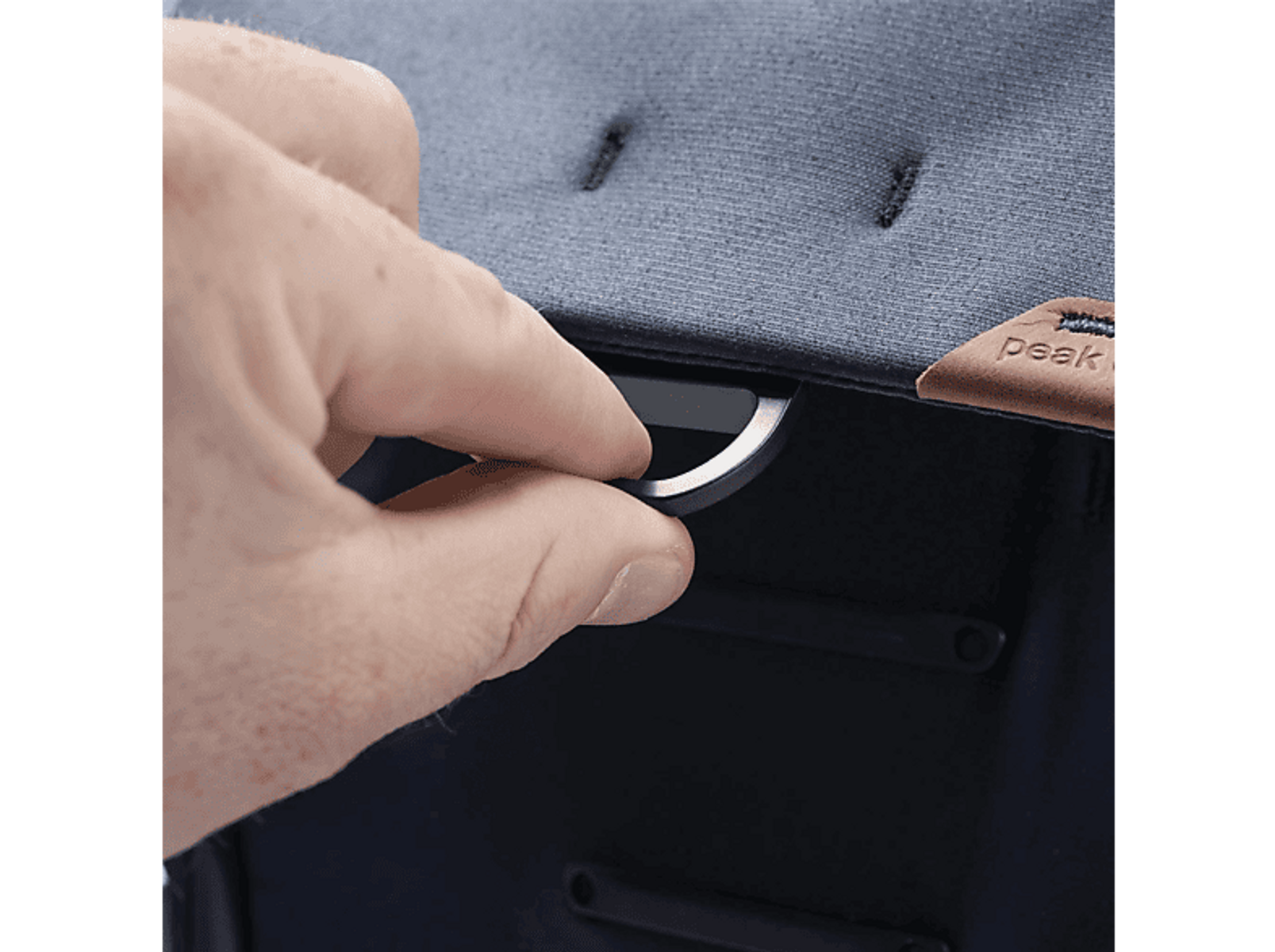 Hand öffnet eine schwarze Peak Design Tasche. Dunkelblauer Stoff, braunes Lederdetail.