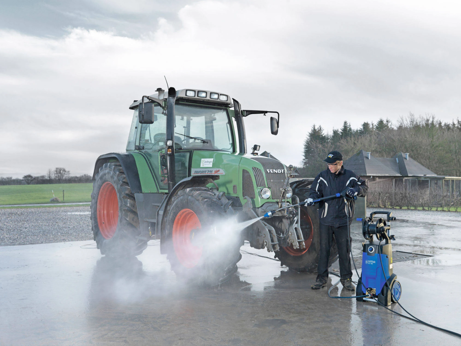 Eine Person reinigt mit einem Hochdruckreiniger einen grünen Traktor.