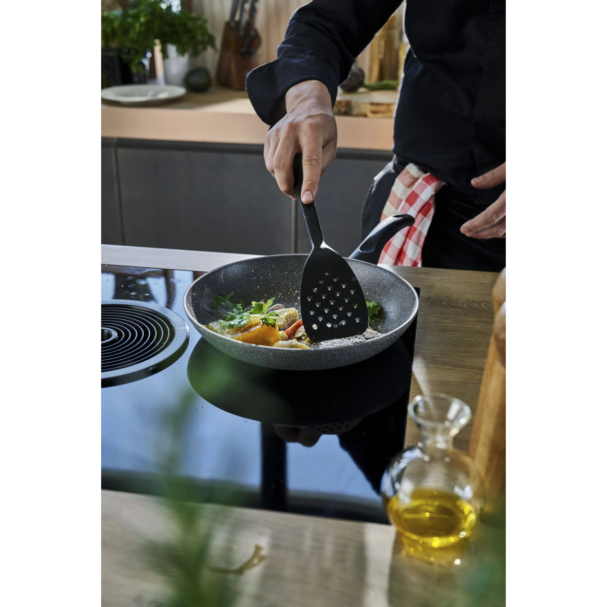 Osoba gotująca na patelni. Szpatułka przewraca jedzenie, widoczny olej i inne składniki.