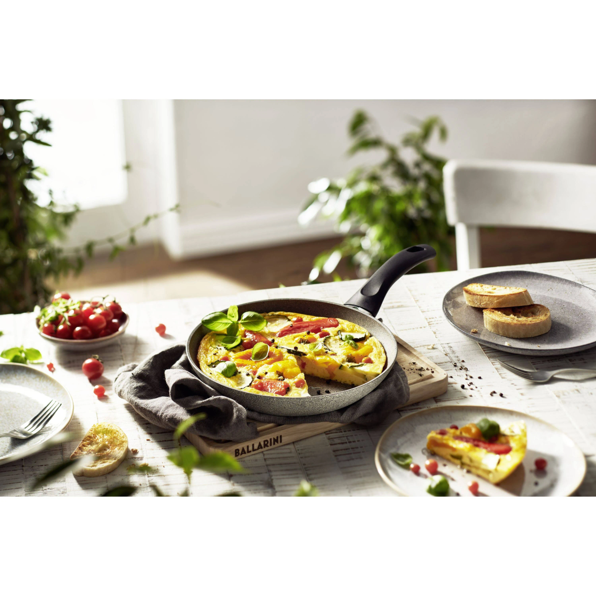 Frittata w patelni na stole. Są pomidory, chleb i talerze. Tłem jest pokój.