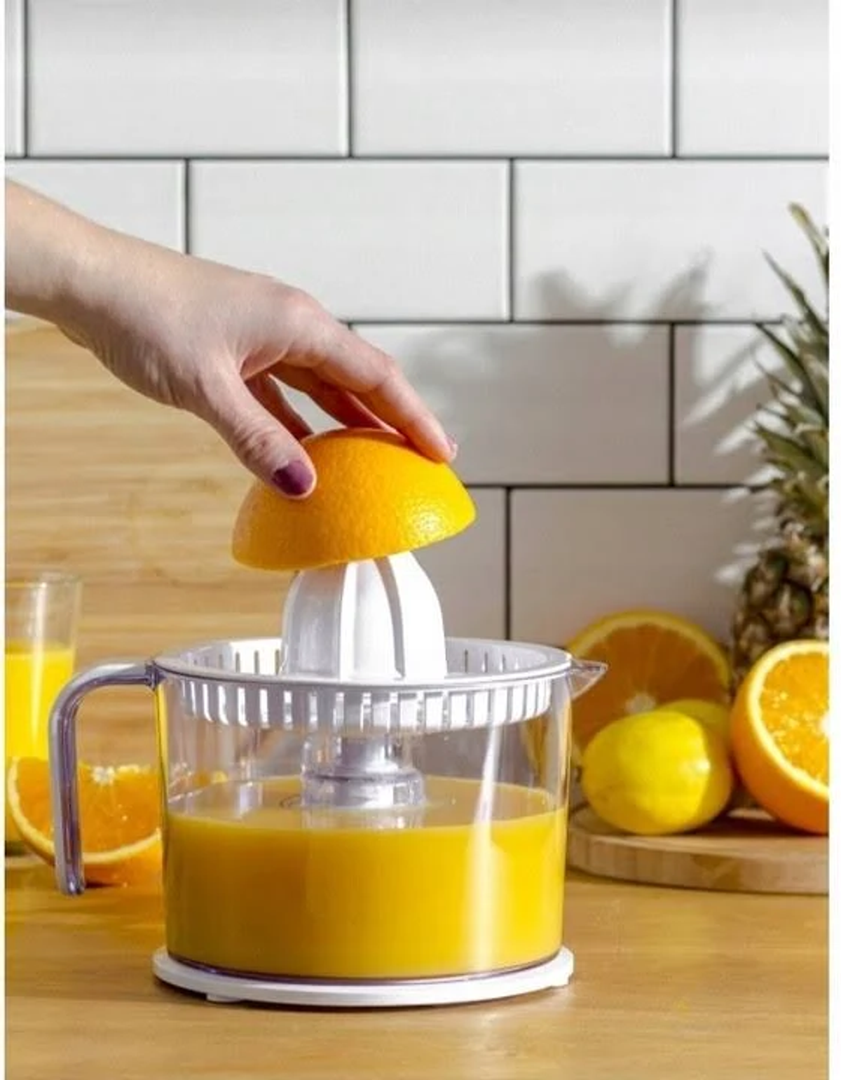 Eine Person, die eine halbe Orange in eine Saftpresse drückt. Saft darin. Holztisch.