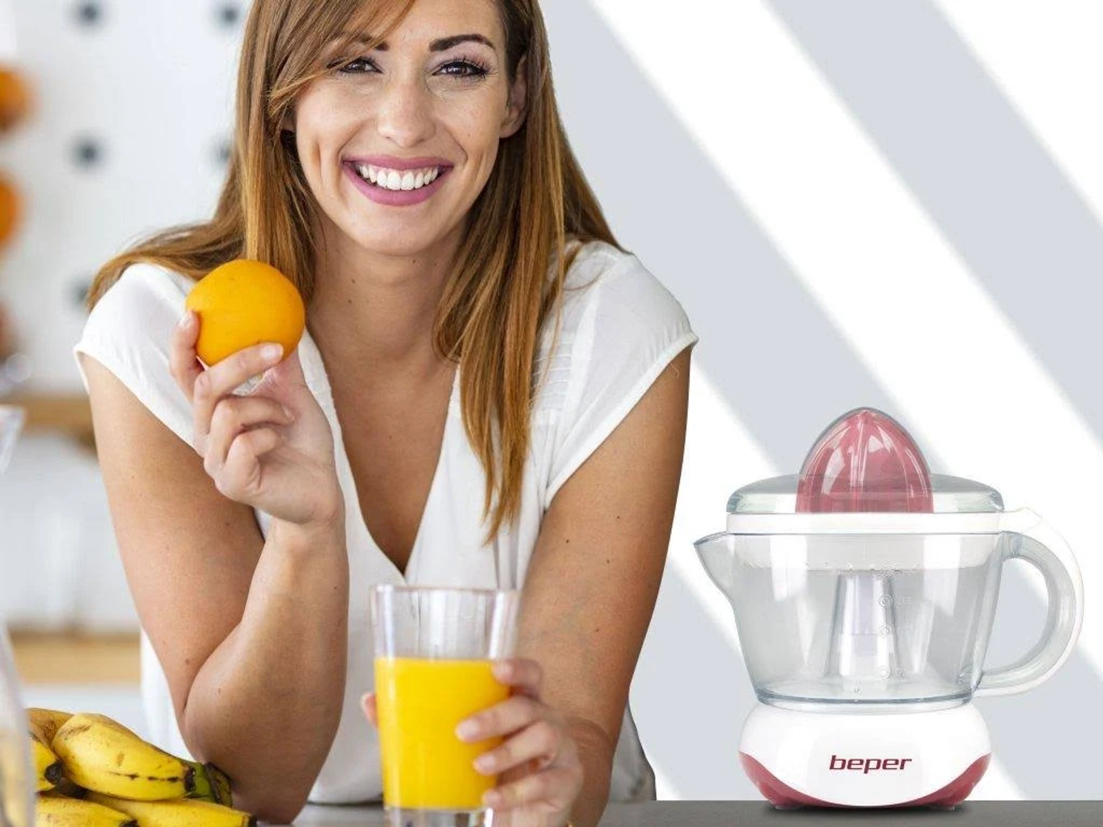 Una donna sorridente, con un'arancia, un bicchiere di succo e uno spremiagrumi vicino.