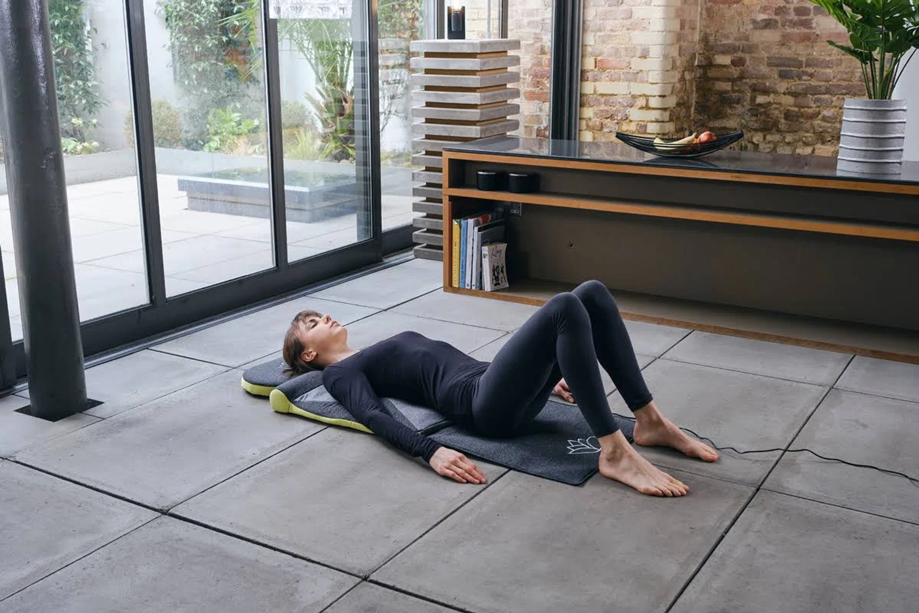 Frau liegt auf einer Yogamatte, Hände an den Seiten, drinnen.