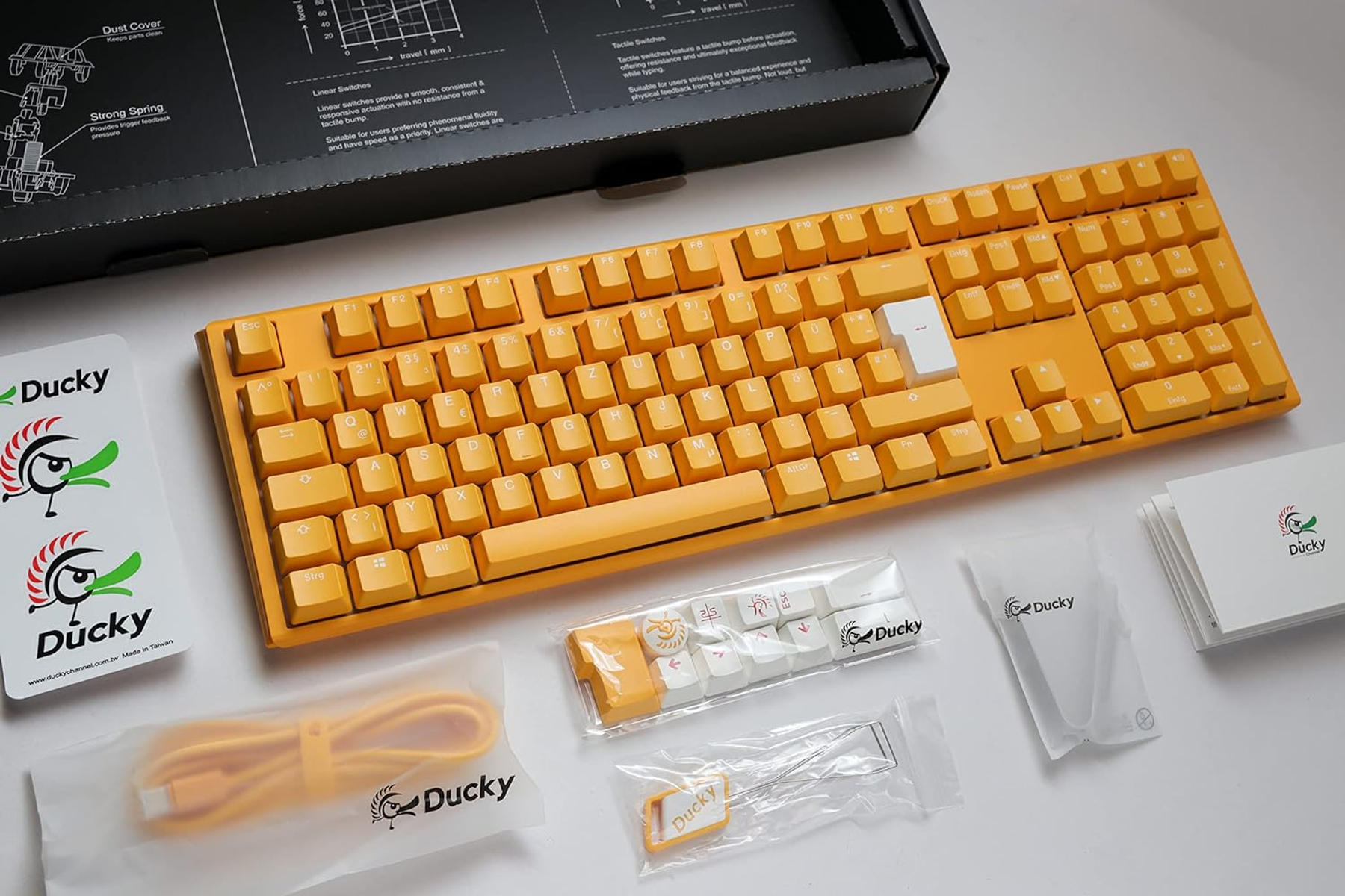 Tastiera Ducky gialla e accessori. Vari oggetti su una superficie bianca.