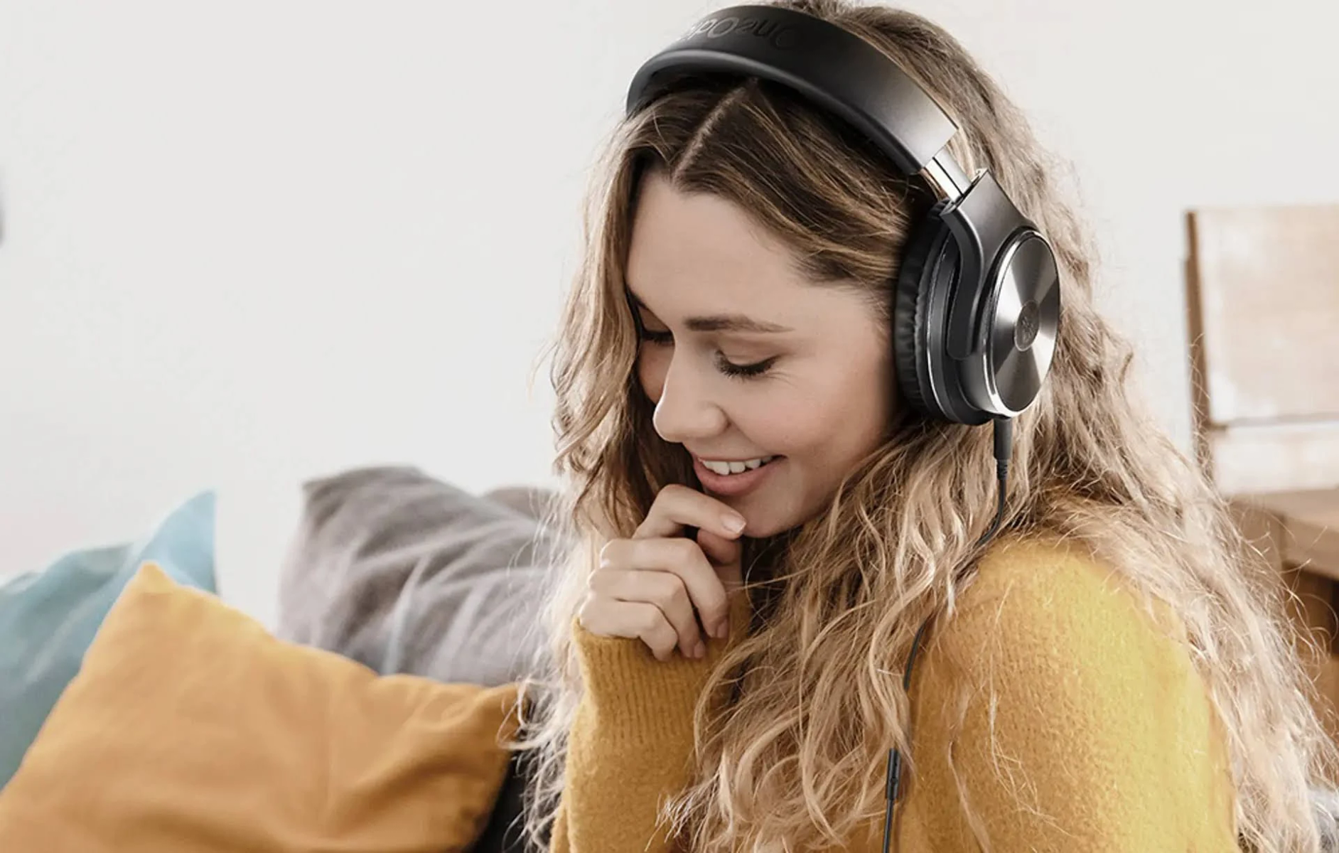 Donna con cuffie, sorridente, seduta su un divano, ascoltando musica.