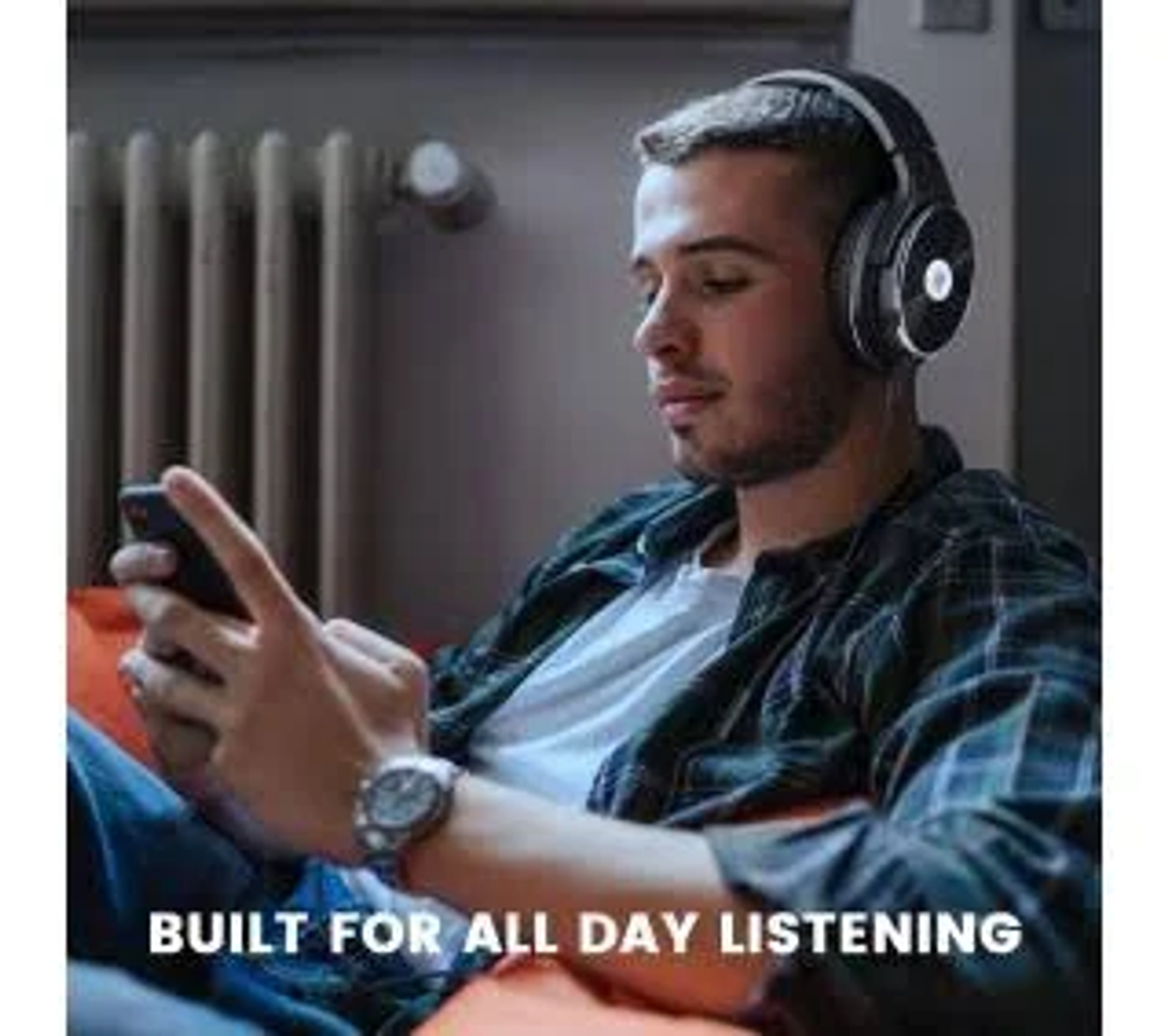 Un uomo con le cuffie tiene in mano un telefono. È seduto su un divano con il testo sottostante: 'BUILT FOR ALL DAY LISTENING'.