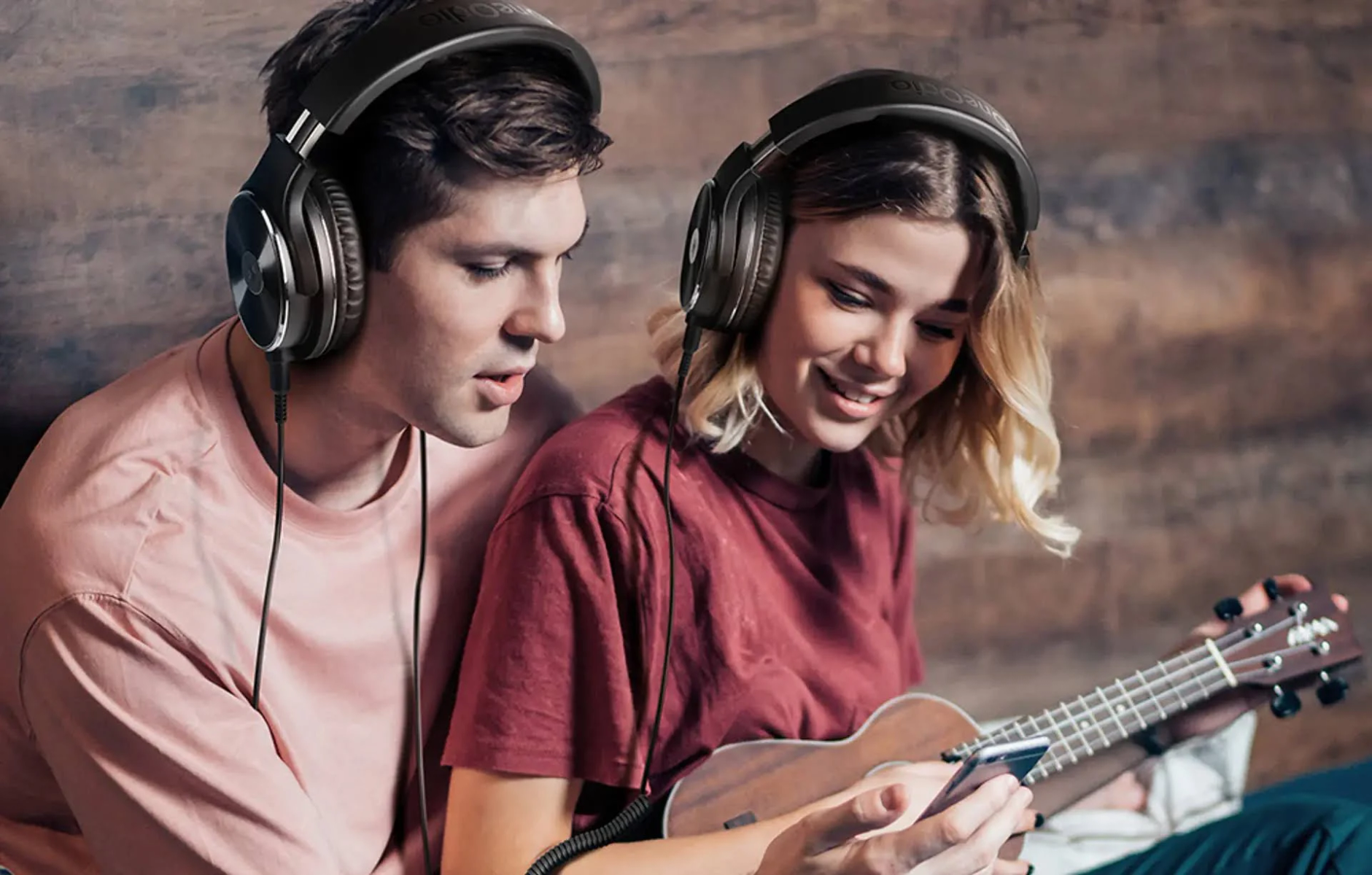 Un uomo e una donna con le cuffie guardano un telefono, con un ukulele vicino.