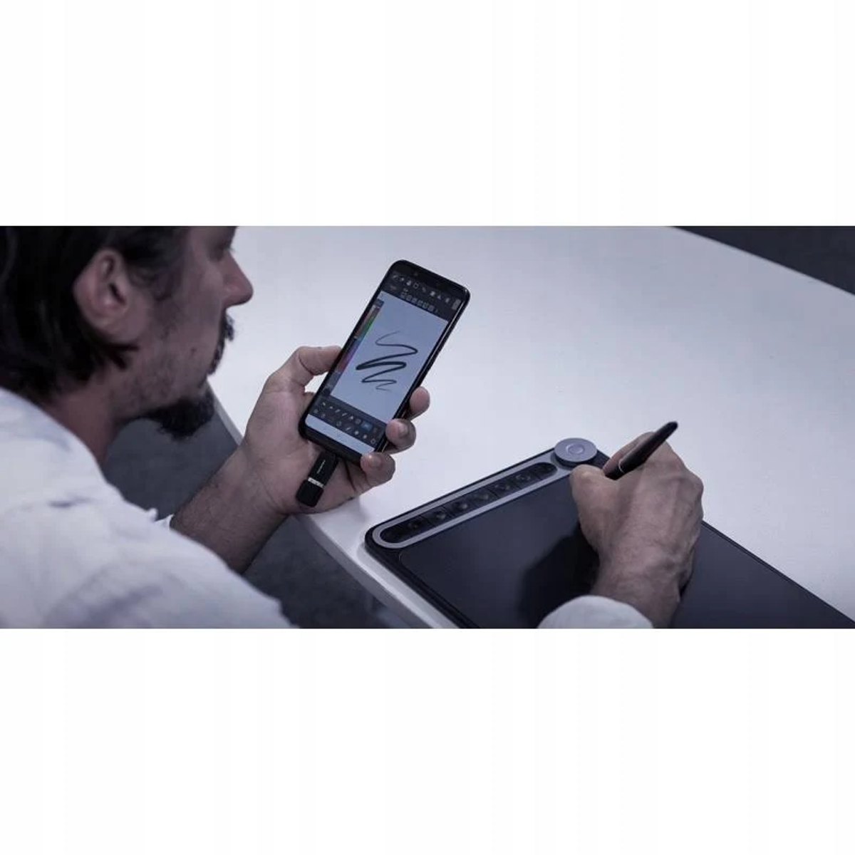 Mężczyzna trzymający telefon, używający rysika na cyfrowym tablecie graficznym.