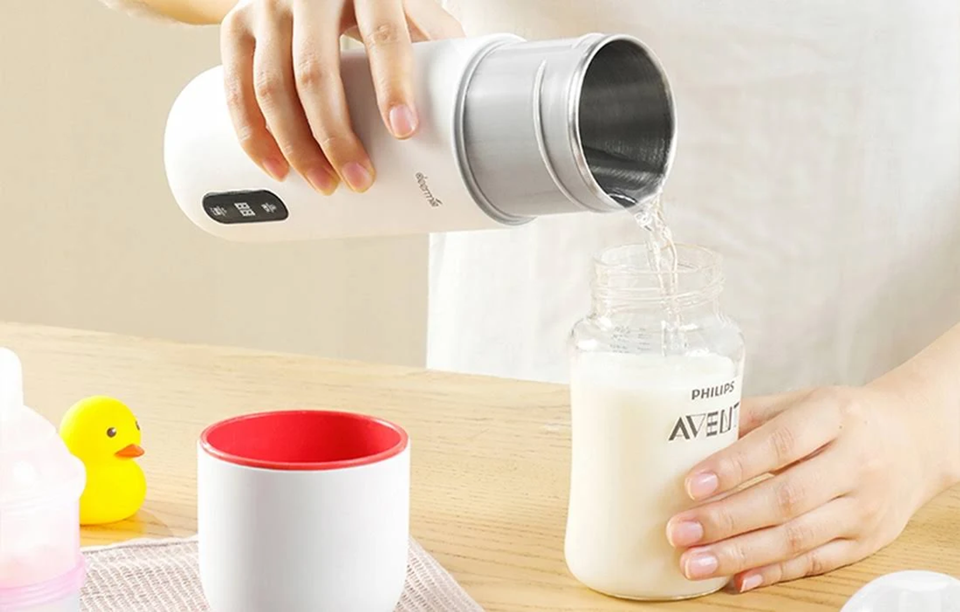 Kobieta nalewa wodę z białej butelki do butelki dla dziecka z mlekiem. Widoczne są inne akcesoria dla dzieci.