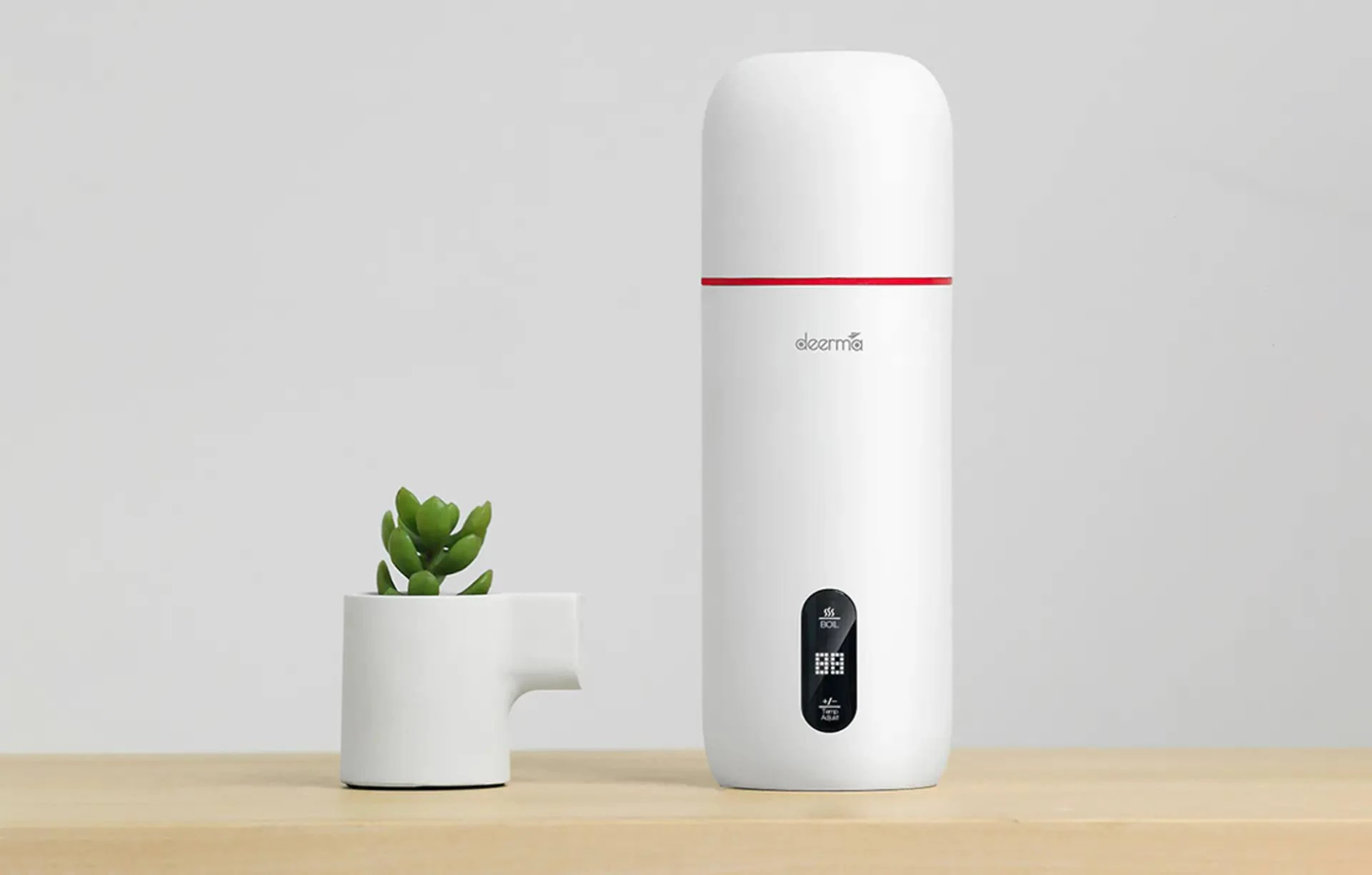 Biały czajnik podróżny i mała roślina na drewnianej powierzchni, neutralne tło.