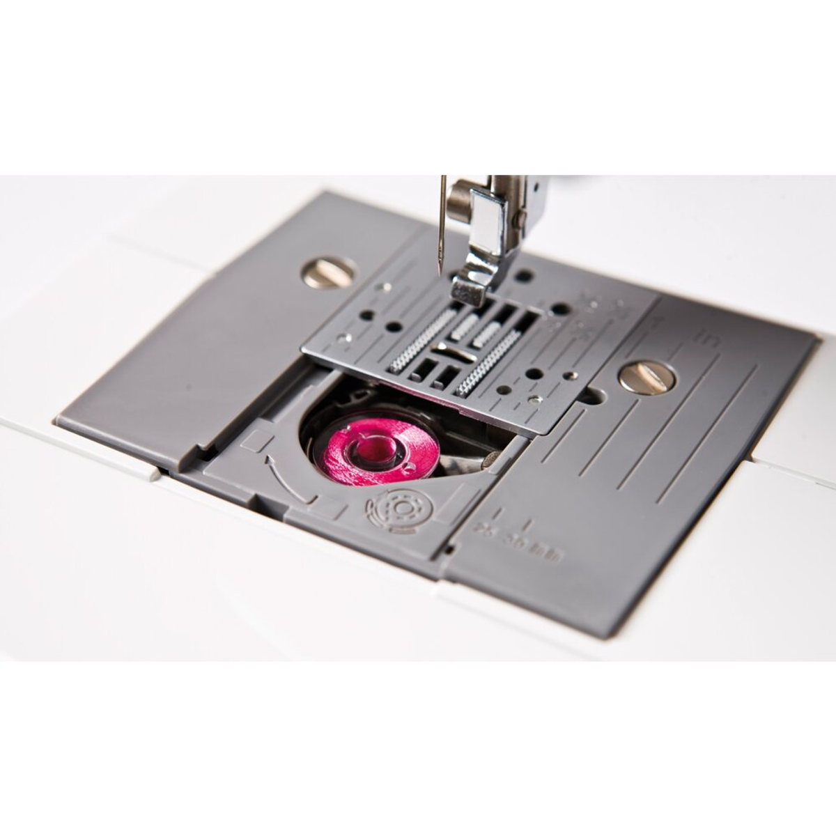 Zbliżenie maszyny do szycia. Igła nad różową szpulką.