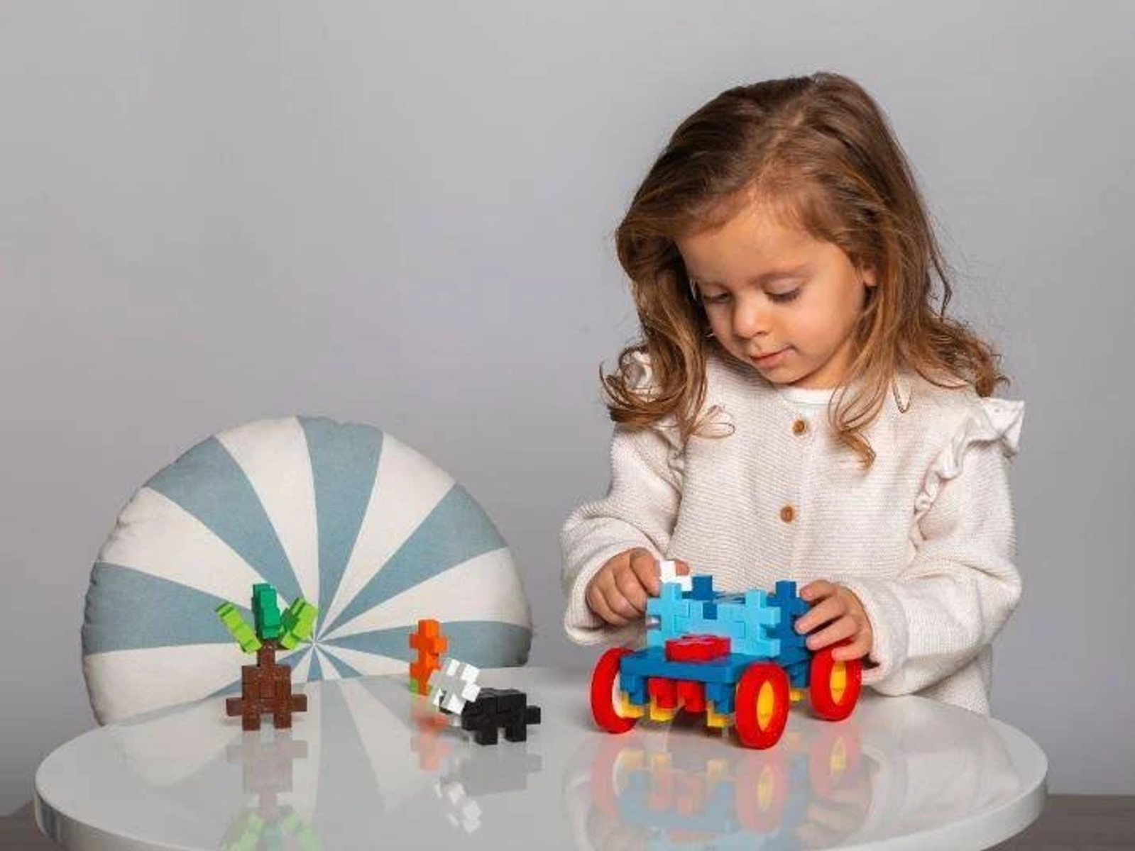 Niña jugando con bloques de construcción. Bloques en mesa con almohada. Fondo gris.