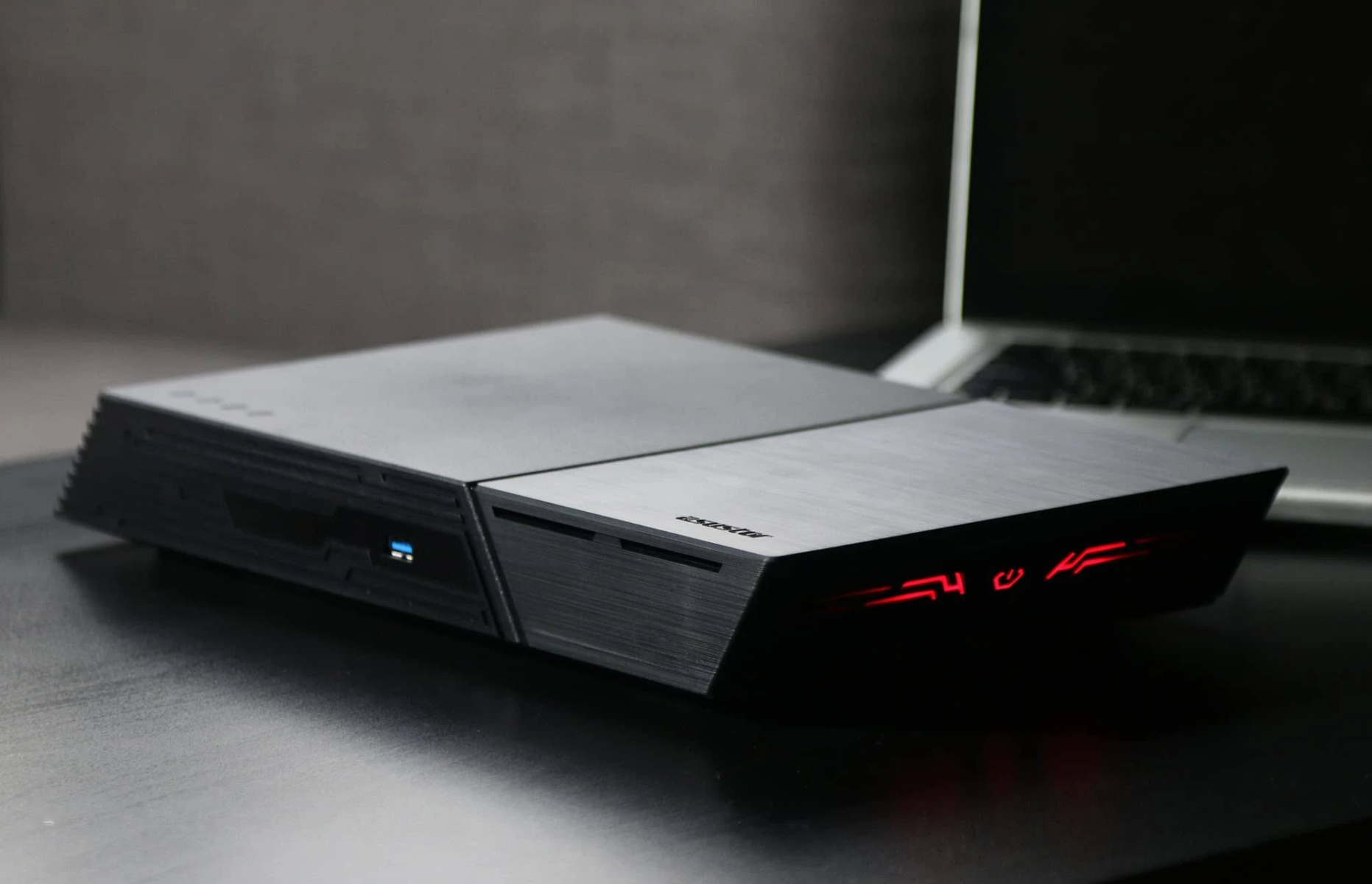 Schwarzes NAS-Gerät auf einem Schreibtisch neben einem Laptop. Das Gerät hat einen USB-Anschluss und rote Akzente.