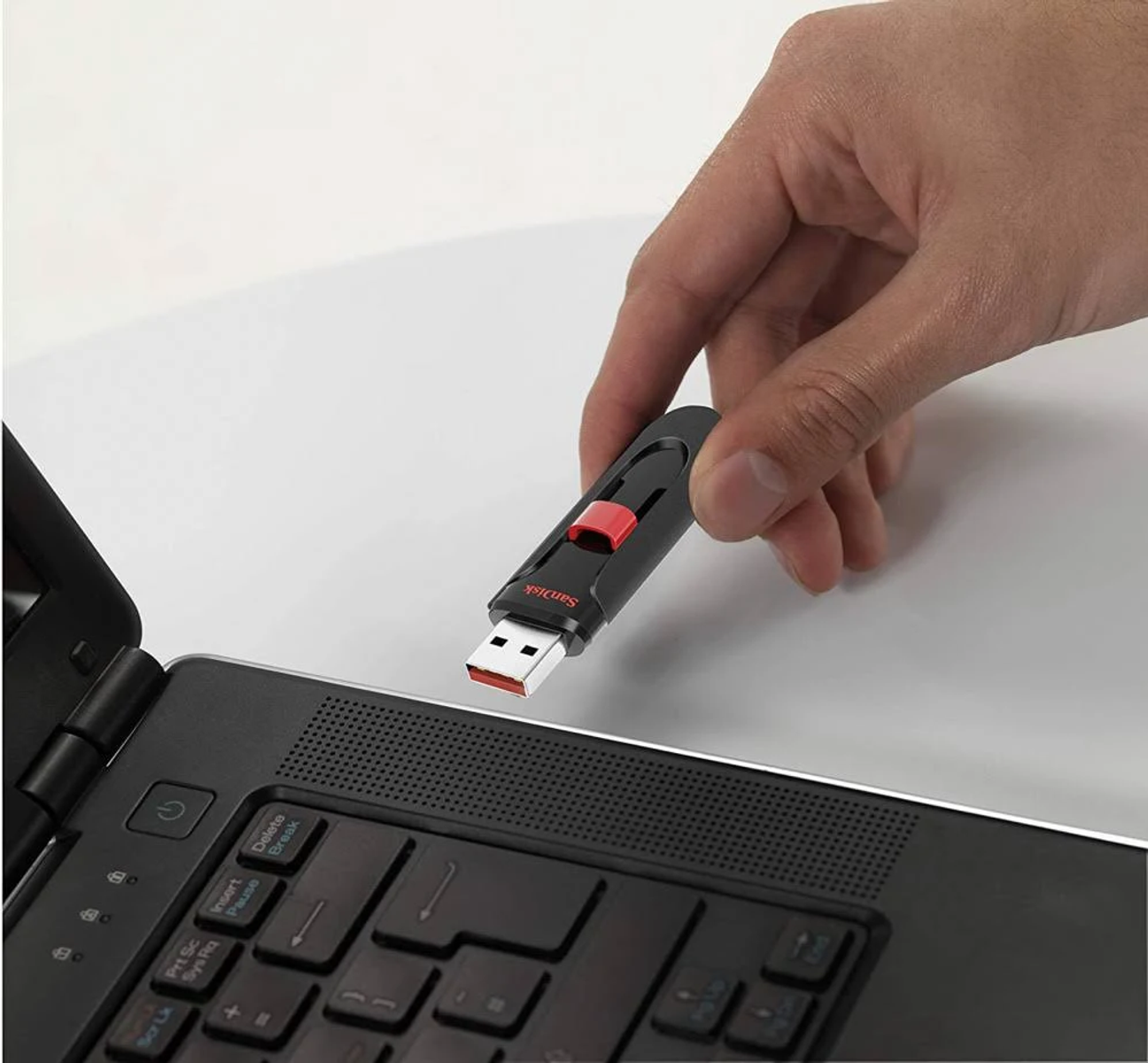 Mano che inserisce una chiavetta USB nera e rossa in un laptop. Superficie bianca.