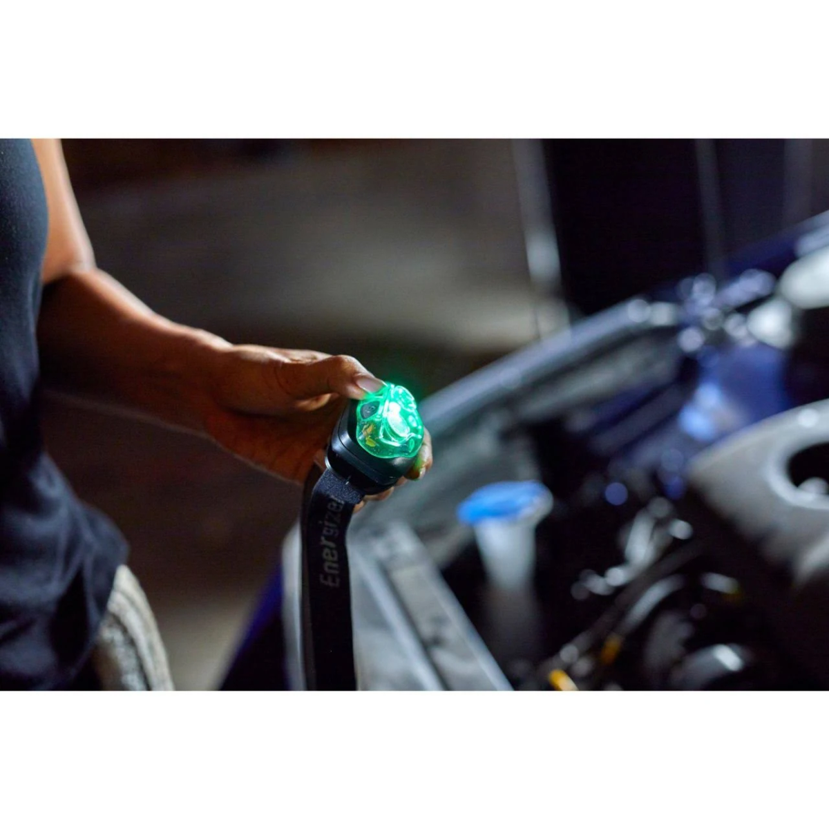 Eine Hand hält eine grüne Energizer-Stirnlampe in der Nähe eines Automotors, dunkler Hintergrund.