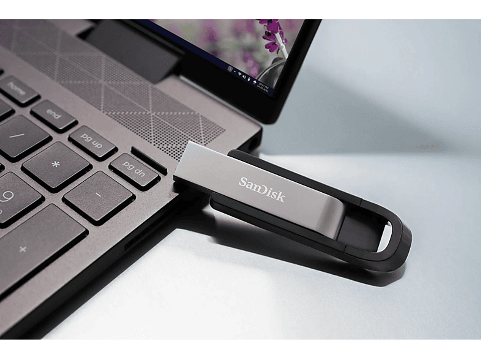 Pendrive USB SanDisk jest włożony do laptopa. Dysk jest czarny i srebrny.