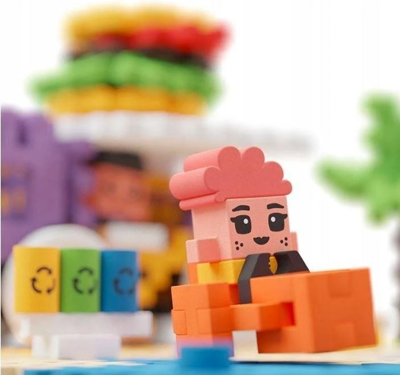 Figurka Lego w pomarańczowej koszuli. Są burgery Lego, palma i scena na plaży.