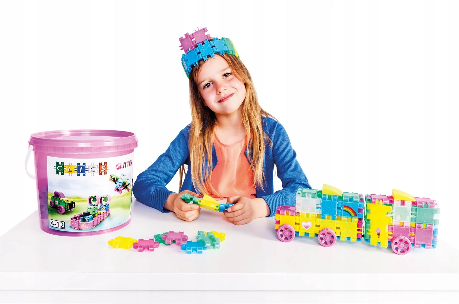 Une fille avec des blocs et jouets colorés, un seau rose et un train jouet sur une table blanche.