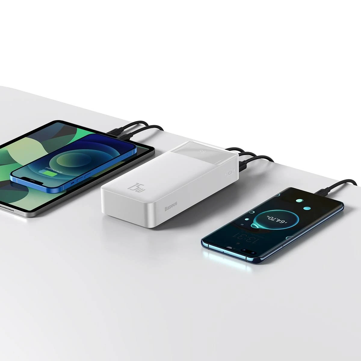 Un banco de energía blanco cargando tres dispositivos: una tableta y dos teléfonos.