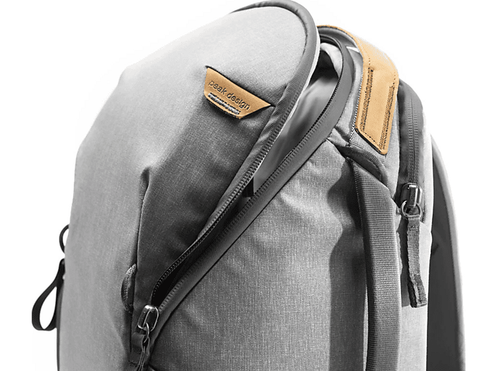 Primo piano di uno zaino grigio con cerniera e un'etichetta Peak Design in pelle marrone.